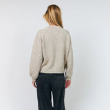 A woman viewed from behind wearing a light beige knit sweater and dark charcoal wide-leg corduroy pants, standing against a plain light gray studio background.
