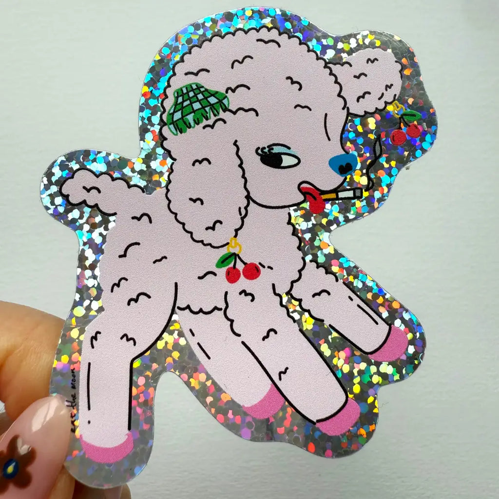 Sticker of a pink poodle with colorful glittery border held by a hand against a light gray background