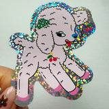 Sticker of a pink poodle with colorful glittery border held by a hand against a light gray background