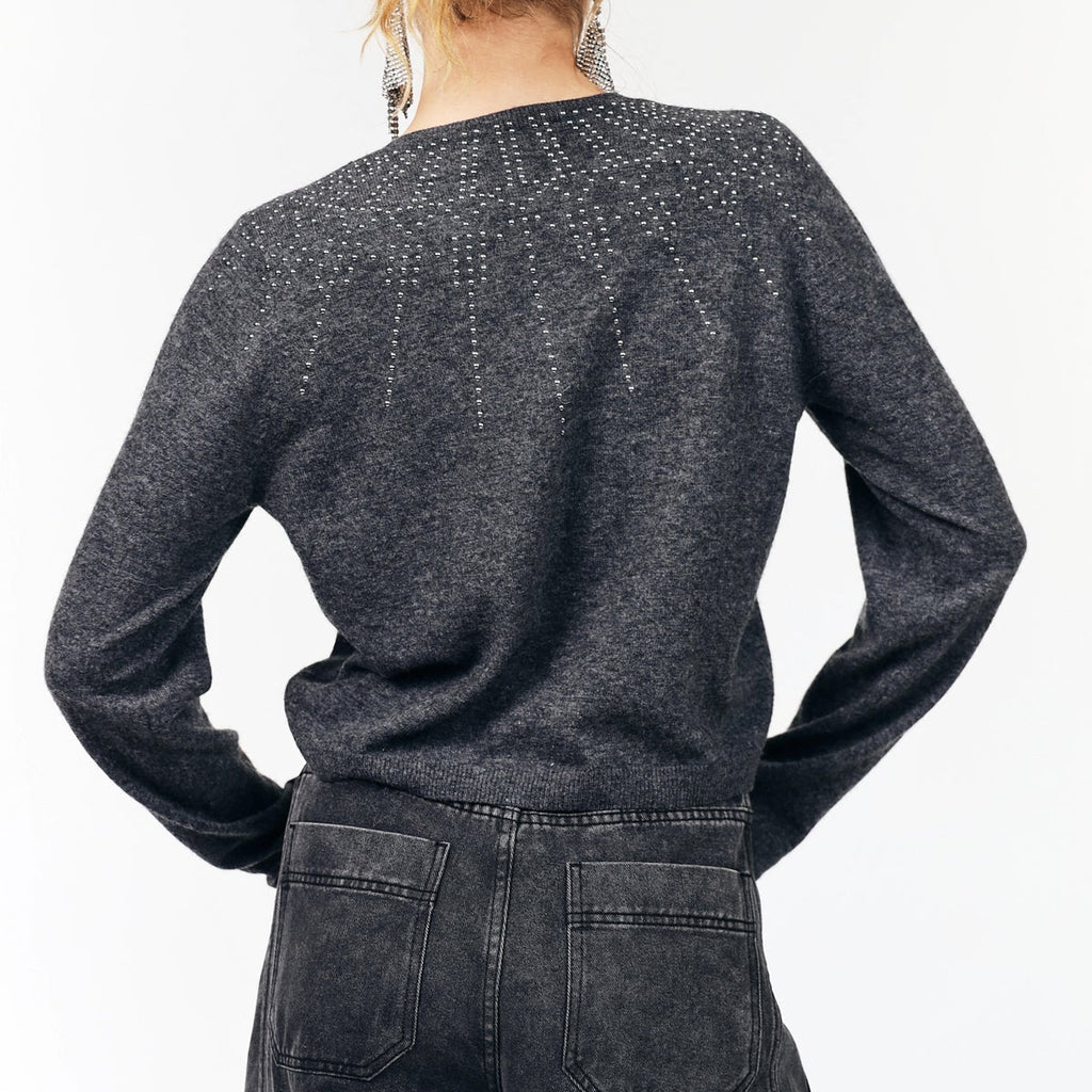 A woman viewed from the back wearing a dark charcoal gray knit sweater with subtle dotted and dashed geometric patterns across the upper back and shoulders, paired with dark gray jeans.