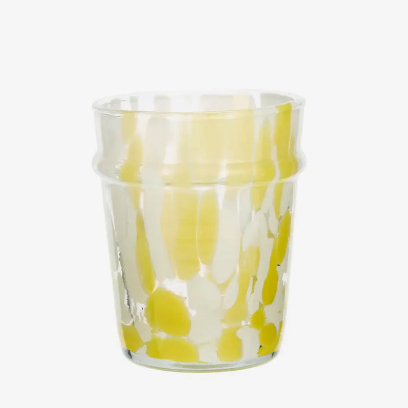 Clear glass tumbler with yellow and white abstract pattern on a white background