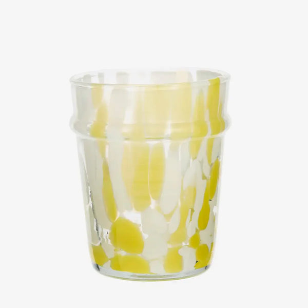 Clear glass tumbler with yellow and white abstract pattern on a white background