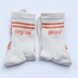 A pair of off-white crew socks with orange stripes and text reading 'negrói' and 'please' on the front, displayed flat against a light background.