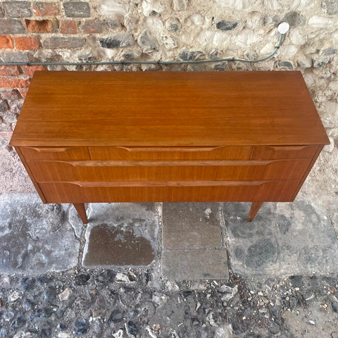 files/Mid-century_modern_wooden_sideboard_with_a_warm_reddish-brown_finish_featuring_two_drawers_with_curved_front_panels_and_tapered_legs_set_against_a_rustic_stone_wall_and_stone_floor..jpg