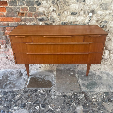 files/Mid-century_modern_wooden_sideboard_with_three_drawers_and_tapered_legs_photographed_outdoors_against_a_stone_and_brick_wall..jpg