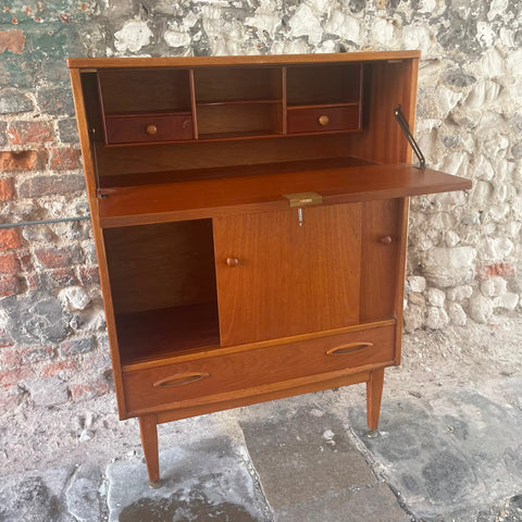files/Mid-century_modern_wooden_writing_desk_cabinet_with_open_shelving_a_pull-out_desktop_two_lower_drawers_and_a_lockable_door_shown_against_a_rustic_stone_and_brick_wall..jpg