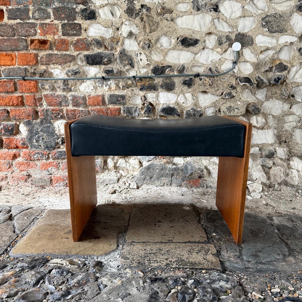 Wooden bench with black cushion against a stone wall.