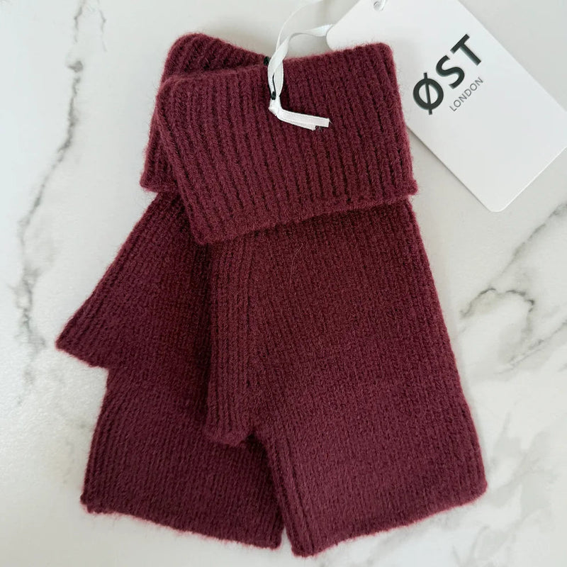 Pair of maroon knit fingerless gloves with a visible brand tag on a marble surface
