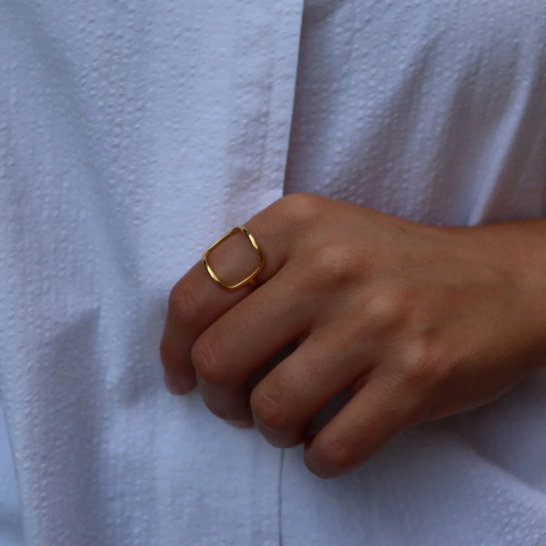 A close-up of a person's hand wearing a thin gold ring, resting on a textured white button-up shirt.