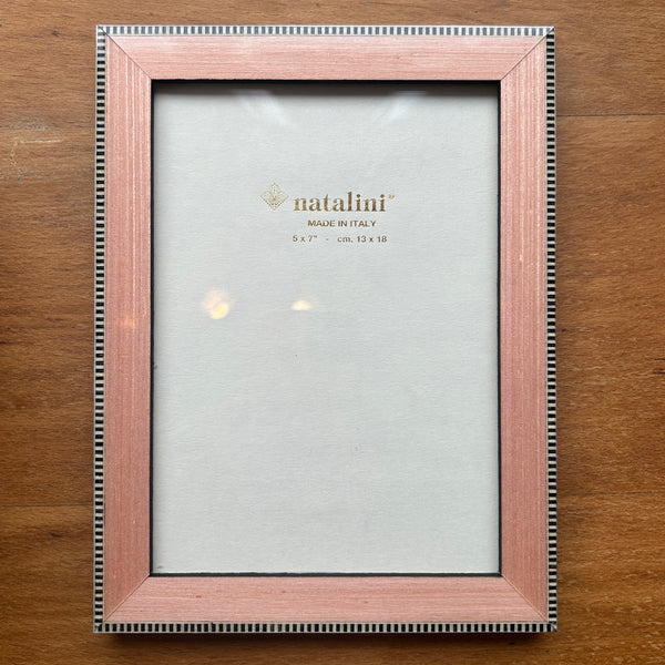 A rectangular picture frame with a light pink wood finish and a silver beaded border, shown empty on a wooden tabletop. The insert card is visible inside the frame, showing the brand name 'natalini'.