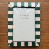 A rectangular picture frame with alternating dark green and cream horizontal stripes, shown on a wooden tabletop. The inside of the frame has a blank white insert with the brand name 'natalini' printed on it.