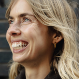 Close-up of a woman with blonde hair and a gold earring, smiling outdoors.