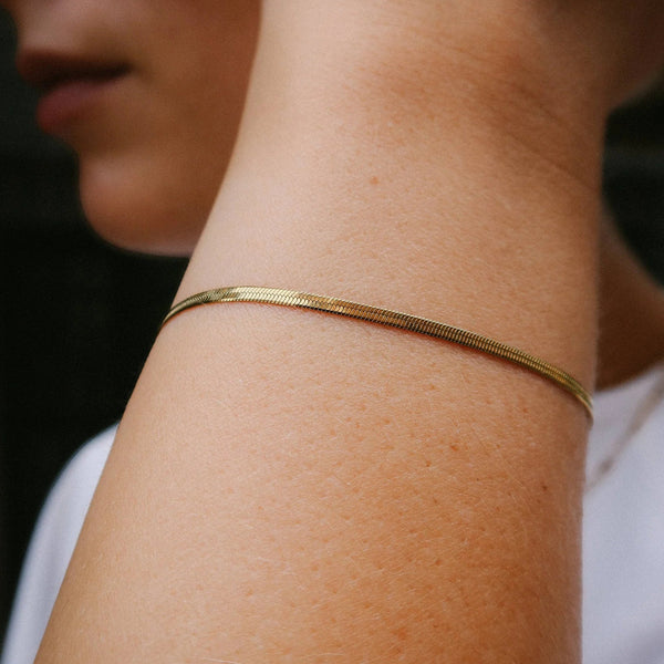A close-up of a person's inner wrist wearing a thin, textured gold chain bracelet.