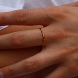 A close-up of a person's hand resting on their leg, wearing a delicate, thin gold ring on one finger.