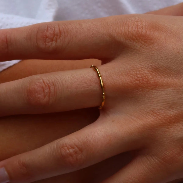 A close-up of a person's hand resting on their leg, wearing a delicate, thin gold ring on one finger.