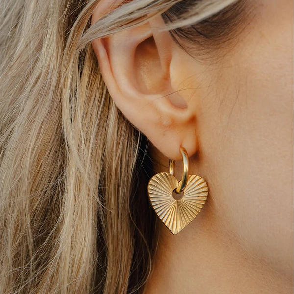 Close-up of a person wearing a gold heart-shaped earring with a blurred background