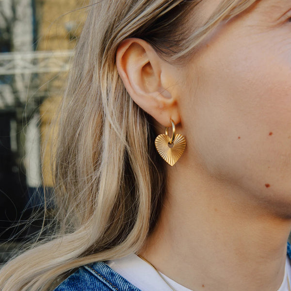 Close-up of a person wearing gold hoop earrings with a blurred background