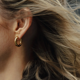 Close-up of an ear wearing a gold hoop earring with blurred hair in the foreground