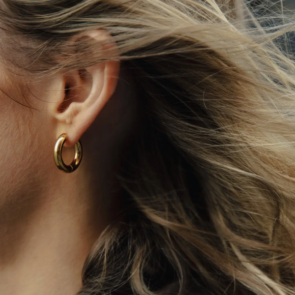 Close-up of an ear wearing a gold hoop earring with blurred hair in the foreground