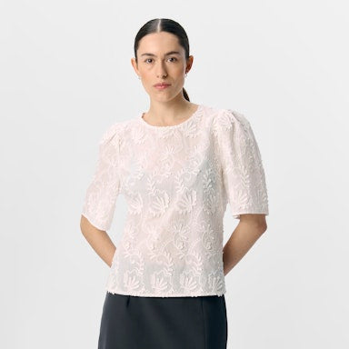 A lady wearing a embroidered white 2/4 top on a white background