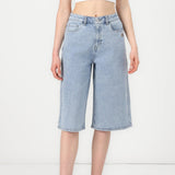 A model wearing light-wash blue denim culottes with a straight, relaxed fit and a raw hem, paired with white high-top sneakers against a plain white studio background.