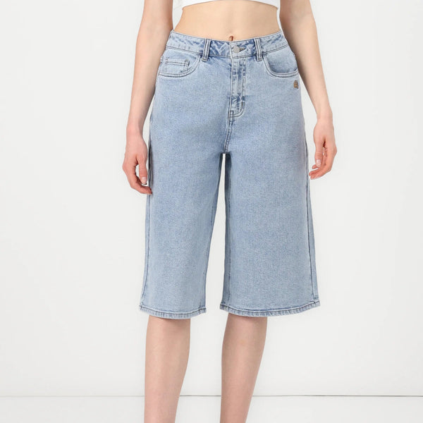 A model wearing light-wash blue denim culottes with a straight, relaxed fit and a raw hem, paired with white high-top sneakers against a plain white studio background.