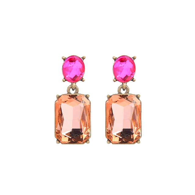 A pair of gold-tone drop earrings featuring a vibrant pink oval gemstone at the top and a peach-colored rectangular emerald-cut gemstone below, set against a plain white background.
