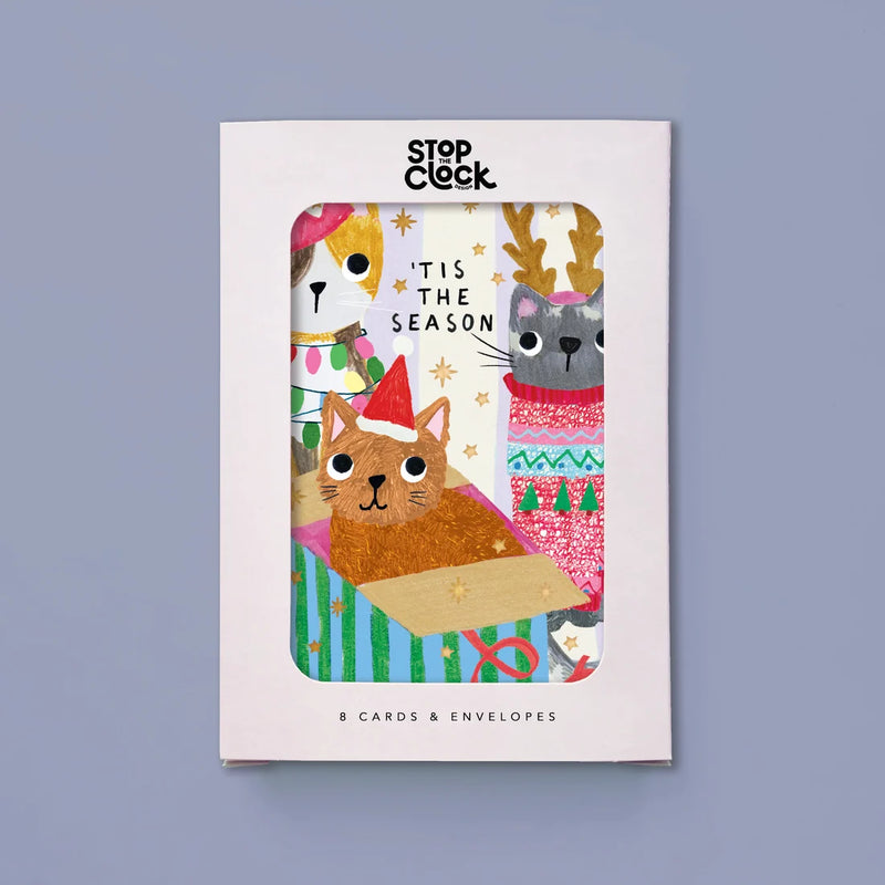 A boxed card set from Stop Clock featuring a festive Christmas illustration with cats, reindeer, and holiday text, shown against a muted blue-gray background.