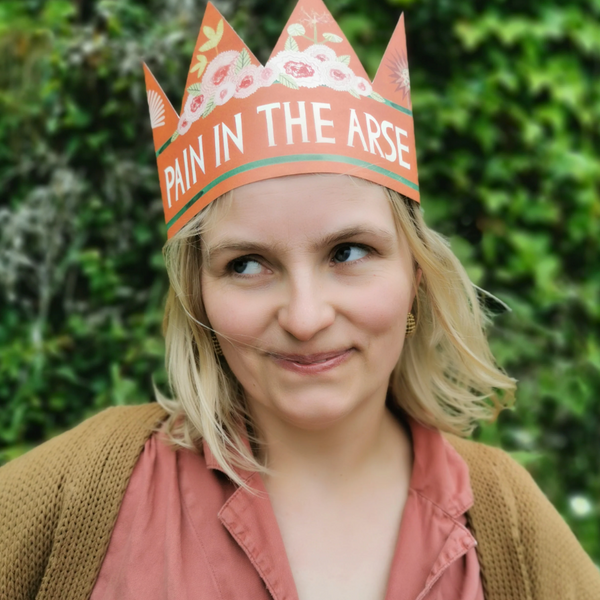 Person wearing a paper crown with text "Pain In The Arse"