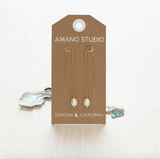 Pair of pearl earrings on a 'Amano Studio' branded card with a white background