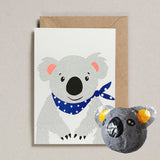 Greeting card with a koala illustration and a small paper mache koala beside it on a neutral background.