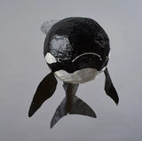 Black and white paper mache orca whale sculpture on a gray background