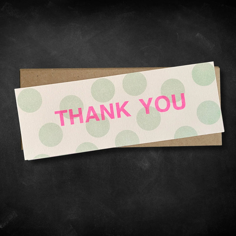 Card with 'THANK YOU' text on a polka dot pattern with a brown envelope on a dark background