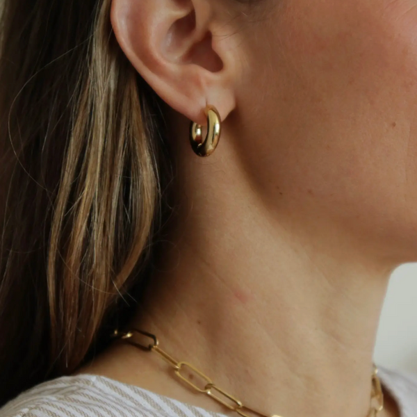 Close-up of a person wearing gold hoop earrings and a gold chain necklace.