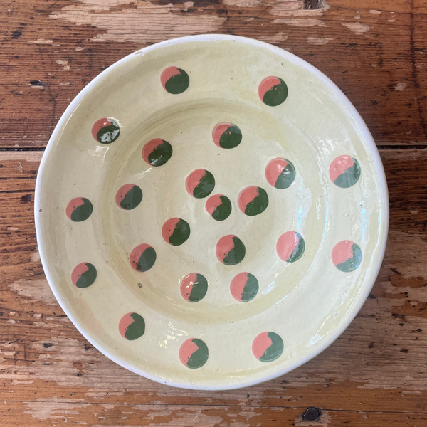Ceramic bowl with green and pink polka dots on a wooden surface