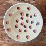 Ceramic bowl with black and pink circular patterns on a wooden surface
