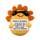 Crocheted sun character with sunglasses holding a sign with motivational text on a white background