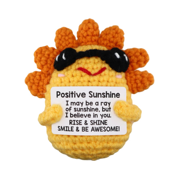 Crocheted sun character with sunglasses holding a sign with motivational text on a white background