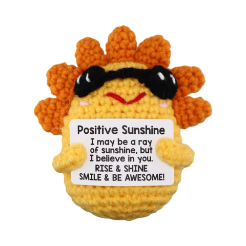 Crocheted sun character with sunglasses holding a sign with motivational text on a white background