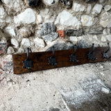 Wooden coat rack with hooks against a stone wall.