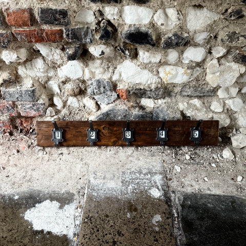 Wooden coat rack with five hooks against a textured stone wall.