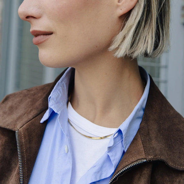 Close-up of a person wearing a brown jacket over a blue shirt with a blurred background