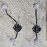 Two decorative wall hooks with curved dark metal arms, square ornate centers, and round textured sball tips, shown on a light wood surface next to a wooden ruler for scale.crackle glazed grey 