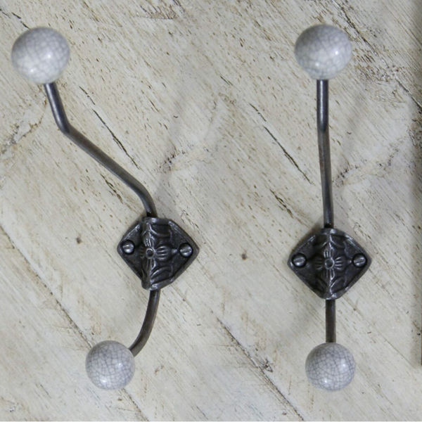 Two decorative wall hooks with curved dark metal arms, square ornate centers, and round textured sball tips, shown on a light wood surface next to a wooden ruler for scale.crackle glazed grey 