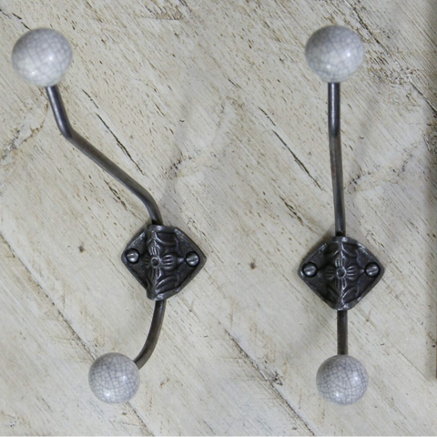 Two decorative wall hooks with curved dark metal arms, square ornate centers, and round textured sball tips, shown on a light wood surface next to a wooden ruler for scale.crackle glazed grey 