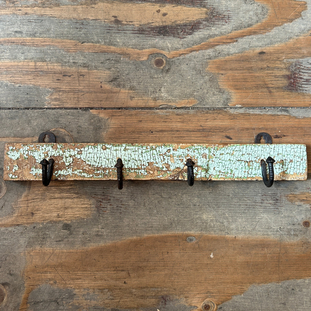 A rustic wooden wall hook rack with five black metal hooks, mounted on a weathered wood plank wall.
