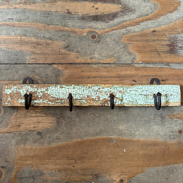 A rustic wooden wall hook rack with five black metal hooks, mounted on a weathered wood plank wall.