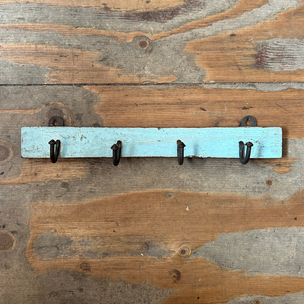 A rustic light blue wooden wall hook rack with four black metal hooks, mounted on a weathered wood plank wall.