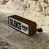 Rectangular device with 'SILENCE' and 'RADIO' text on a stone surface and stone wall background