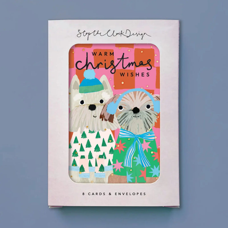 A boxed card set titled 'Warm Christmas Wishes' by Stop the Clock Design, featuring an illustrated window view of two dogs in holiday clothing on a pink patterned background, with '8 Cards & Envelopes' printed below.